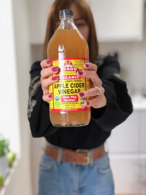 Woman Holding Bragg Apple Cider Vinegar In Air